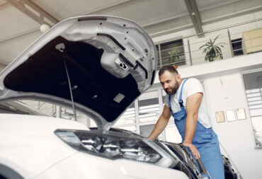 Wrker in a car salon. Expert checks the car. Man in a blue uniform.